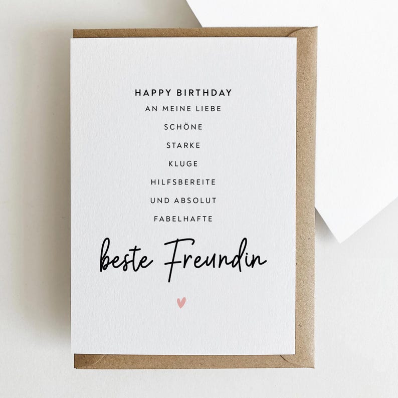 May include: A white greeting card with the words "Happy Birthday" and other German phrases in black text. The card is in a brown envelope, with a small pink heart at the bottom.