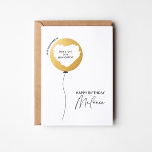 Könnte beinhalten: Eine weiße Geburtstagskarte mit einem goldenen Ballon-Design und dem Text "Happy Birthday Melanie". Die Karte enthält den Text "Hier steht dein Wunschtext" im Ballon. Die Karte befindet sich in einem braunen Umschlag.