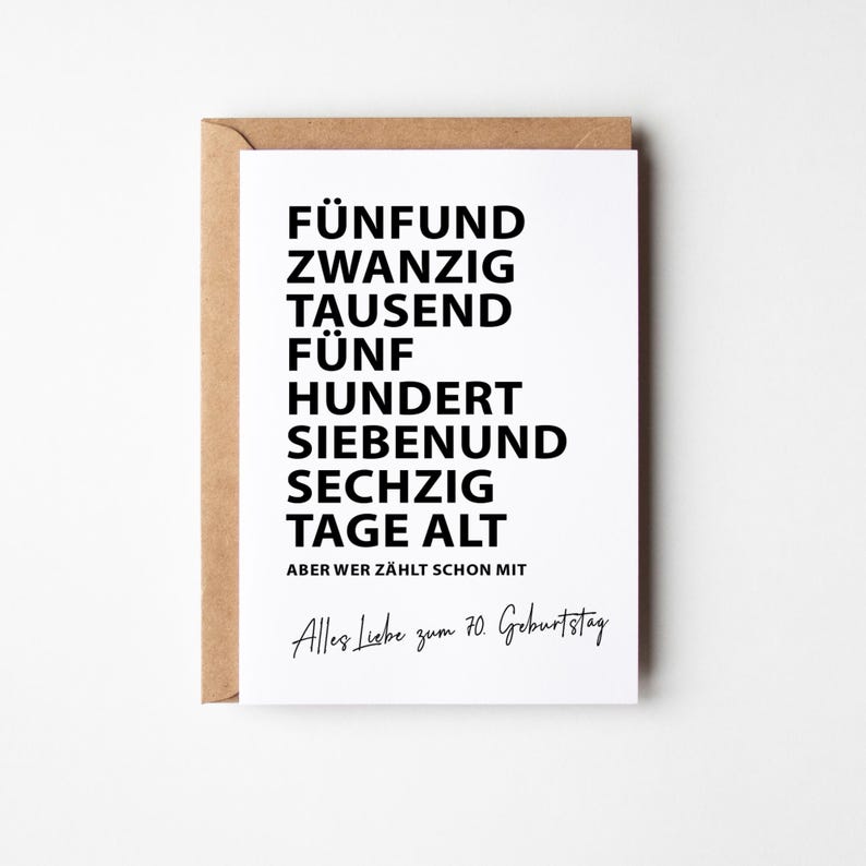 K&ouml;nnte beinhalten: Eine wei&szlig;e Gru&szlig;karte mit schwarzem Text, pr&auml;sentiert in einem braunen Umschlag. Der Text der Karte lautet "F&Uuml;NFUND ZWANZIG TAUSEND F&Uuml;NF HUNDERT SIEBENUND SECHZIG TAGE ALT" und "Alles Liebe zum 70. Geburtstag."
