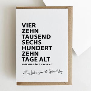 K&ouml;nnte beinhalten: Eine wei&szlig;e Gru&szlig;karte mit schwarzem Text in einem braunen Umschlag. Die Karte lautet "VIER ZEHN TAUSEND SECHS HUNDERT ZEHN TAGE ALT" und "Alles Liebe zum 40. Geburtstag".