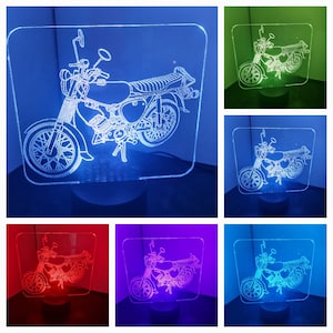 Könnte beinhalten: Eine weiße Umrandung eines Motorrads auf einem klaren Acrylsockel mit einem hellblauen, grünen, roten, violetten und weißen LED-Licht. Das Motorrad ist im Vintage-Stil mit einem Einzelsitz und einem hohen Lenker.