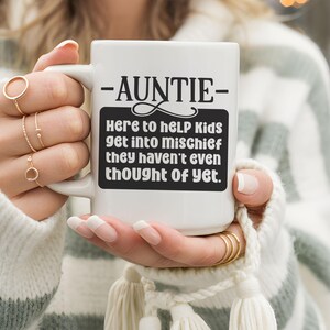 Könnte beinhalten: Weiße Keramik-Tasse mit dem Wort "-AUNTIE-" oben und einem schwarzen Rechteck mit dem Text "Here to help Kids get into mischief they haven't even thought Of yet."
