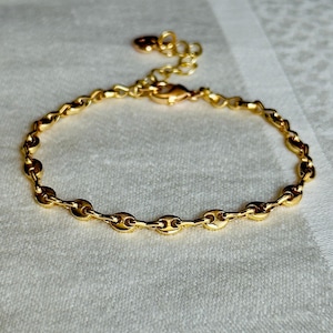 Op de afbeelding: Een goudkleurige armband met een schakelontwerp. De armband heeft een reeks kleine, verbonden schakels, met een karabijnsluiting en een verstelbare ketting. De sieraden worden op een wit oppervlak gepresenteerd.