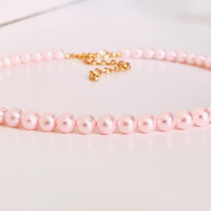 Può includere: Una delicata collana di perle rosa con catena e chiusura color oro. La collana presenta piccole perle rotonde rosa chiaro. La chiusura è un design semplice ed elegante. Un classico gioiello.
