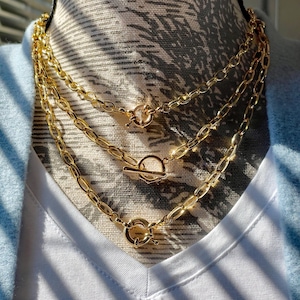 May include: A set of three gold chain necklaces with toggle clasps. The chains are layered on a white mannequin.