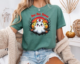 May include: A teal green t-shirt featuring a cartoon ghost wearing a nurse's hat and holding a pumpkin. The text "Boo Boo Squad" is above the ghost.