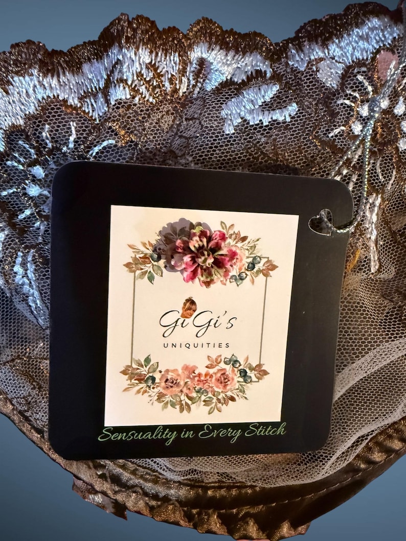 Pu&ograve; includere: Una scheda quadrata nera con il testo "GiGi's Uniquities" e "Sensuality in Every Stitch" &egrave; mostrata. La scheda &egrave; decorata con un disegno floreale. La scheda &egrave; ambientata su uno sfondo di pizzo intricato, marrone e bianco.