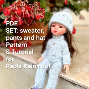 Op de afbeelding: PDF-patroon en tutorial voor een blauwe gebreide trui, broek en muts set voor een Paola Reina pop. De pop draagt de set en zit op een stenen trede.