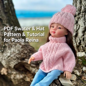 Könnte beinhalten: Ein rosa gestricktes Pullover- und Mützenset für eine Puppe. Der Pullover hat ein Zopfmuster und einen Rollkragen. Die Mütze hat einen Bommel oben. Das Set ist für Paola Reina Puppen konzipiert. PDF Swater & Hat Pattern & Tutorial for Paola Reina.
