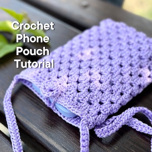 May include: A purple crocheted phone pouch with a drawstring closure. The pouch is lying on a wooden surface. Crochet Phone Pouch Tutorial.