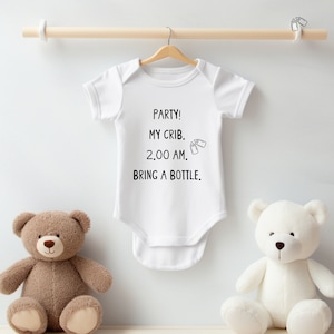 Może przedstawiać: Biały śpioszek dla niemowlęcia z czarnym tekstem, kt&oacute;ry brzmi "Party! My Crib. 2:00 AM. Bring a Bottle." Dwie małe czarne ikony butelek znajdują się obok tekstu "2:00 AM".