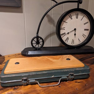 Könnte beinhalten: Eine vintage grüne Metallwerkzeugbox mit einem Holzdeckel und einem schwarzen Metallgriff. Die Werkzeugbox steht auf einer Holzoberfläche neben einer schwarzen Uhr mit römischen Ziffern.