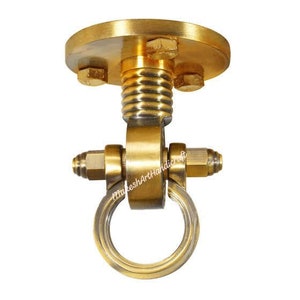 Puede incluir: Un gancho de techo de metal dorado con una base redonda y un anillo giratorio. El gancho está diseñado para colgar objetos del techo.