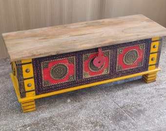 May include: A wooden storage chest with a yellow, red, and black painted design. The chest has a hinged lid and decorative metal accents. It sits on four short legs.