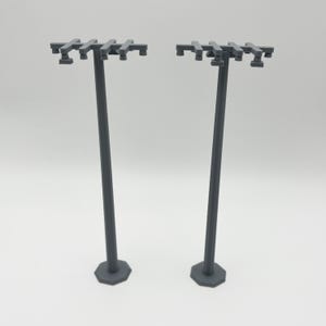 Op de afbeelding: Twee grijze plastic model nutsmasten met dwarsbalken en isolatoren. De masten zijn ongeveer 25 cm hoog en hebben een zeshoekige basis.
