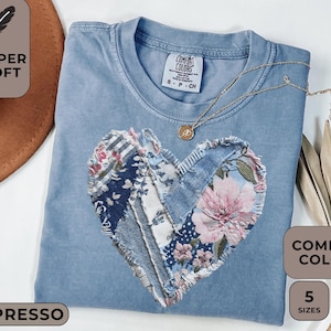 May include: A light blue Comfort Colors t-shirt with a heart-shaped patchwork design. The heart features floral and denim fabrics. A gold necklace with a pendant rests on the shirt. The shirt has the text "Comfort Colors", "Super Soft", "Espresso", "5 Sizes", and "12 Colors".