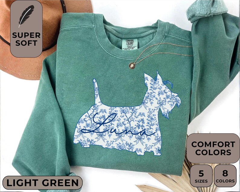 Pu&ograve; includere: Felpa verde chiaro con un motivo floreale a forma di cane e il nome "Luna". La felpa ha un girocollo e maniche lunghe. L'immagine include anche il testo "Super Soft", "Comfort Colors", "Light Green", "5 Sizes" e "8 Colors".