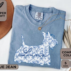 Pu&ograve; includere: T-shirt blu jeans Comfort Colors con un disegno floreale di cane e il nome "Luna". La maglietta ha un girocollo e maniche corte. &Egrave; presente anche il testo "Super Soft", "Comfort Colors", "5 Taglie" e "12 Colori".