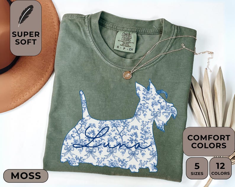Pu&ograve; includere: T-shirt verde muschio con un disegno floreale di cane blu e bianco. Il nome del cane, "Luna", &egrave; scritto in corsivo. La maglietta ha le parole "Super Soft" e "Comfort Colors" stampate sopra. Disponibile in 5 taglie e 12 colori.