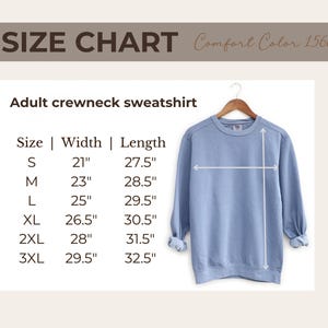 Pu&ograve; includere: Una felpa girocollo blu chiaro per adulti, esposta su una gruccia di legno. L'immagine include una tabella delle taglie con misure in cm per le taglie dalla S alla 3XL. Il testo "SIZE CHART Comfort Color 1566" &egrave; in alto.