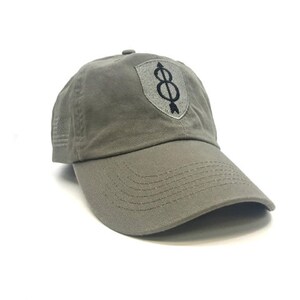 May include: Olive green baseball cap with a curved brim. The cap features a shield-shaped patch with the number 8 and an arrow design. An American flag is embroidered on the side.