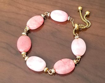 May include: A pink and white gemstone bracelet with a gold chain and clasp. The bracelet has a sliding clasp that allows for adjustable sizing.