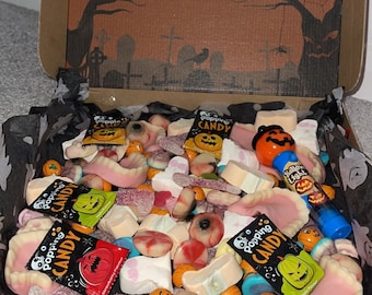 May include: An orange and black Halloween-themed gift box filled with various candies, including gummy teeth, eyeballs, and pumpkin-shaped candies. The box has a black and white spiderweb design and the text "Happy Halloween".