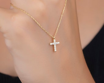 May include: A delicate gold chain necklace with a small, sparkling diamond cross pendant.