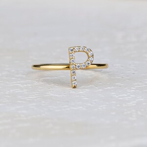 May include: A gold ring with a single letter 'P' made of small diamonds.