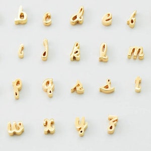 Puede incluir: Una colecci&oacute;n de abalorios dorados con letras min&uacute;sculas del alfabeto, cada uno con una fuente cursiva. Las letras est&aacute;n dispuestas sobre una superficie blanca. Estos abalorios son adecuados para la fabricaci&oacute;n de joyas o manualidades personalizadas.