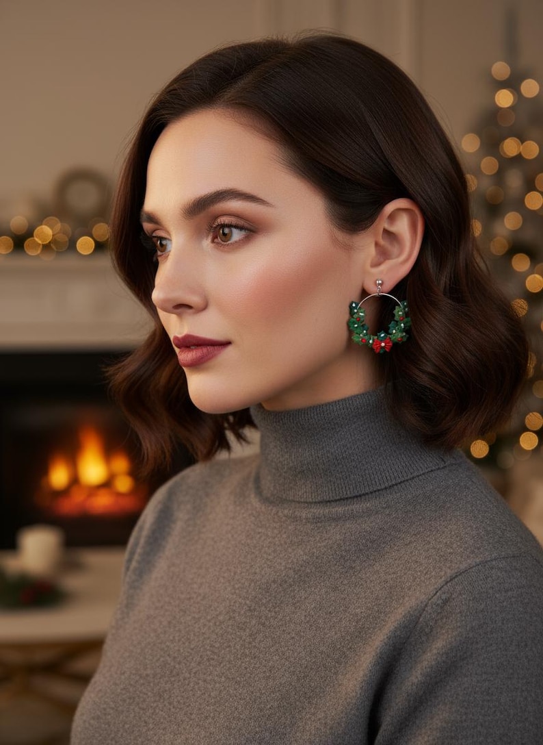May include: A woman wearing a gray turtleneck sweater and hoop earrings. The earrings are decorated with green beads and small red accents, resembling miniature wreaths. The background features a blurred fireplace and Christmas lights.