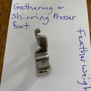 May include: Silver sewing machine foot for gathering or shirring fabric. The foot is labeled "Siman Co Part 121441 Gathering or Shirring Presser Foot".