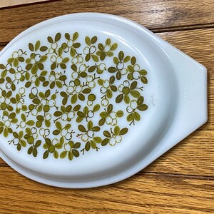 May include: White oval ceramic baking dish with a green and white floral pattern. The pattern features small green leaves and white berries.