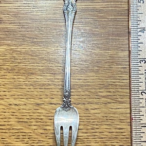 May include: A silver fork with an ornate handle and three tines. The fork is about 6 inches long.