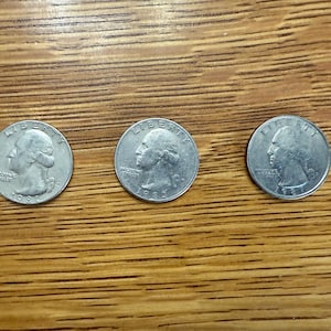 May include: Three silver US quarter dollar coins with the profile of George Washington on the obverse side.