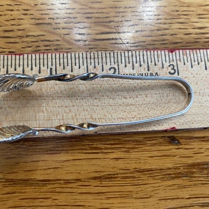 May include: Silver sugar tongs with a twisted design and leaf-shaped ends. The tongs are about 3 inches long and are made in the USA.