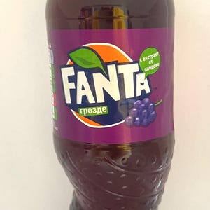 May include: A plastic bottle of grape-flavored Fanta soda. The bottle is purple and has a white label with the Fanta logo and the words "grape" and "with fruit extract".