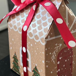 May include: A brown cardboard gift box shaped like a gingerbread house with white icing details and red and white polka dot ribbon.