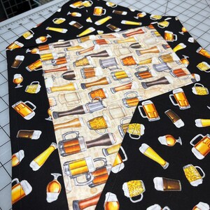 May include: A set of three fabric pieces with beer-themed patterns. The central piece has a beige background with various beer mugs and glasses. The other two pieces have a black background with yellow and brown beer glasses and mugs. The fabrics are likely for crafting or home decor.