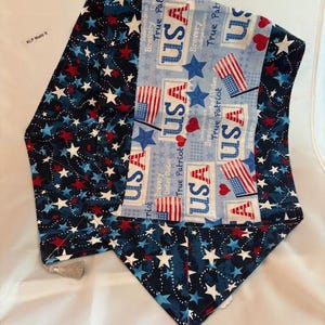 May include: A patriotic table runner with a blue, red, and white color scheme. The runner features star and flag patterns, with the word "USA" prominently displayed. Tassels adorn the ends. The design evokes a sense of American pride and celebration.