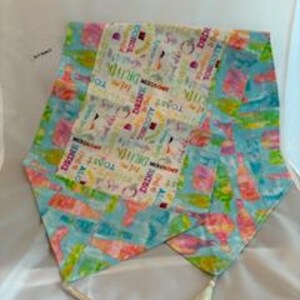 May include: A colorful table runner with a light blue background and a central panel featuring text and images related to drinks and celebrations. The runner has a length of approximately 60 inches and includes tassels at each end.