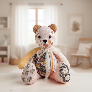 May include: A handmade patchwork teddy bear with a variety of floral and patterned fabrics. The bear features a mix of pink, orange, yellow, and navy blue fabrics. It has a white lace collar and brown striped ears.