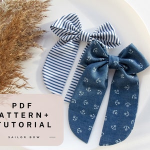 Könnte beinhalten: Zwei Stoffhaarbänder, eines mit weißen Ankern auf blauem Hintergrund und eines mit weißen und blauen Streifen. Der Text "PDF PATTERN + TUTORIAL SAILOR BOW" befindet sich auf einem rosa Hintergrund.