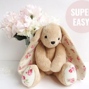 A cute, handmade stuffed bunny plushie sitting in front of a bouquet of peonies. The toy is made from light brown plush fabric with floral fabric accents on its long ears and feet. It is a versatile plush sewing pattern that serves as a bunny sewing pattern, a stuffed bear pattern, or a bear sewing pattern. Perfect for those looking for plushie patterns pdf or toy sewing patterns to make a DIY memorial bear or simply a charming cute animal pattern.