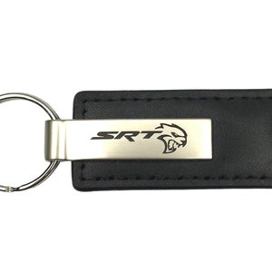 May include: Black leather key chain with a silver metal insert that says "SRT" and has a stylized animal head logo.
