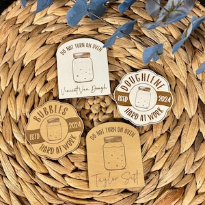 May include: Four wooden jar-shaped signs with text. Two signs read "Do Not Turn On Oven" with names below. One sign says "Bubbles Estd 2024 Hard at Work". The last sign says "Doughlene Estd 2024 Hard at Work".