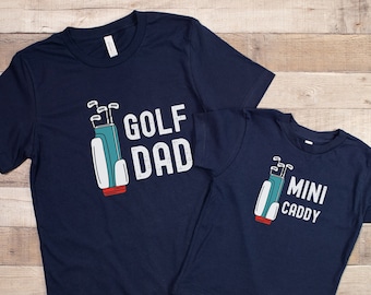 May include: Two navy blue t-shirts with a golf bag and golf club graphic. The larger shirt says "Golf Dad" and the smaller shirt says "Mini Caddy".