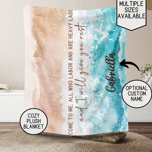 May include: A cozy plush blanket with a watercolor design of ocean waves and a sandy beach. The text "Come to me, all who labor and are heavy lade and I will give you rest." is printed on the blanket. The name "Gabriella" is printed on the bottom right corner of the blanket.