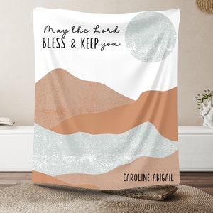 May include: A white tapestry with a beige and blue mountain landscape design. The text "May the Lord bless & keep you." is printed at the top. The name "CAROLINE ABIGAIL" is printed at the bottom.