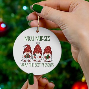 May include: White ceramic Christmas ornament with three gnomes wearing red hats and holding gifts. The ornament reads "NICU NURSES WRAP THE BEST PRESENTS".